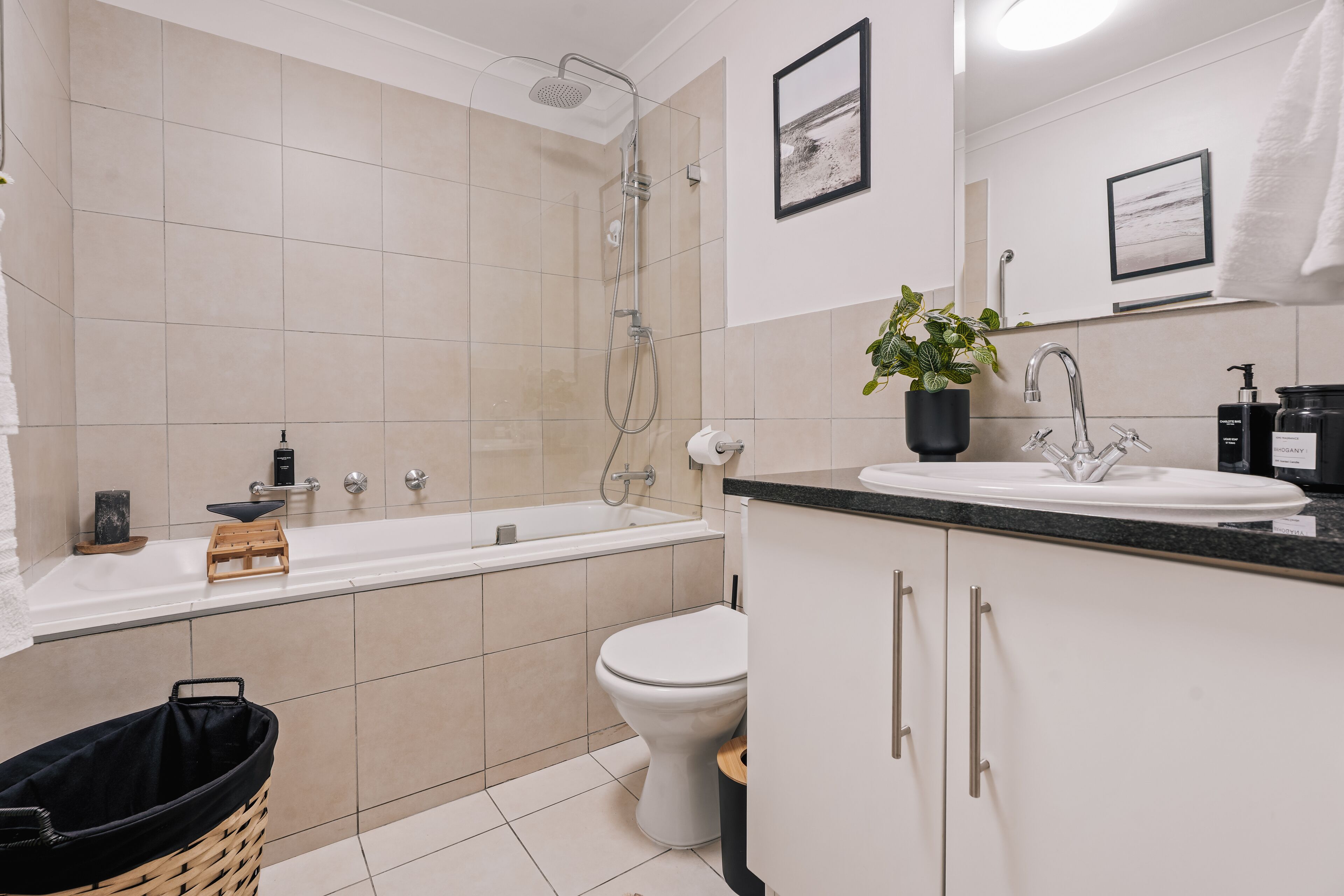 Une salle de bain moderne avec une baignoire, des toilettes et un lavabo. On y trouve une plante sur le comptoir et une poubelle.