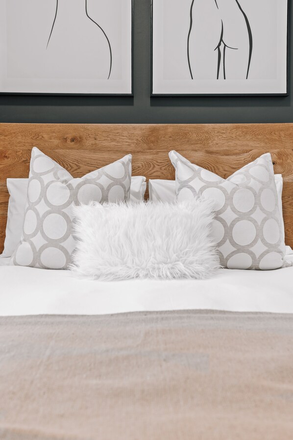 A bed with patterned pillows, a fluffy white pillow, and two framed artworks on the wall above.