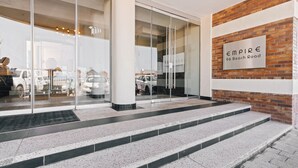 A building entrance with glass doors, a brick wall with a sign, and a set of steps leading up to the entrance.