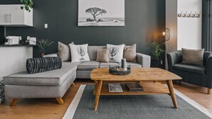 A modern living room with a grey sofa, a wooden coffee table, and a black and white artwork on the wall.