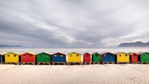 A row of colorful beach huts aligned on a sandy beach with a cloudy sky.