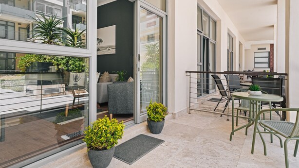 A modern apartment with a balcony, large windows, and a dining area with outdoor seating.