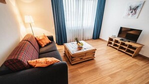 Una sala de estar con sofá, mesa de centro, mueble para televisión y lámpara.