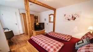 Una habitación acogedora con techo de madera, un televisor sobre un mueble de madera, dos camas con ropa de cama a cuadros, un escritorio pequeño y un espejo.