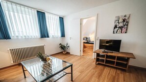 Una sala moderna con una mesa de centro de vidrio, un mueble bajo para televisión de madera y una planta en maceta.