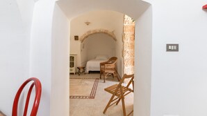 Una habitación con una cama, una silla de mimbre, una mesita y una silla roja.