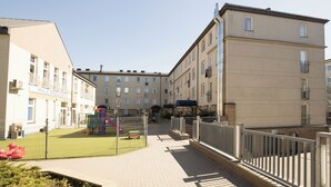 Une cour avec un terrain de jeux, des bâtiments dotés de balcons et un ciel dégagé.