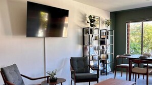 A modern living room with a flat-screen TV, two armchairs, a coffee table, and a bookshelf. - Kalk Bay Secure Seaside Apartment (Cape Town)