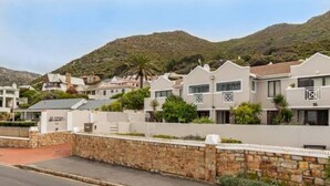 A residential street with houses, a stone wall, and a mountain in the background. - Kalk Bay Secure Seaside Apartment (Cape Town)