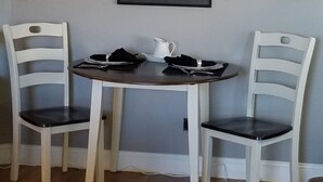 Un comedor con una mesa redonda y dos sillas blancas con asientos negros. Hay una jarra blanca y un servilleta negra sobre la mesa.