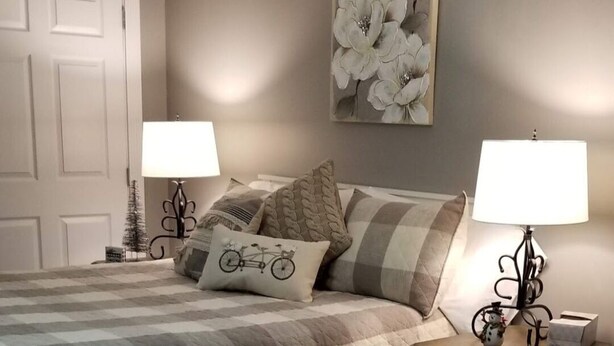 Un dormitorio con una cama grande, dos mesitas de noche con lámparas, un cuadro en la pared y una puerta.
