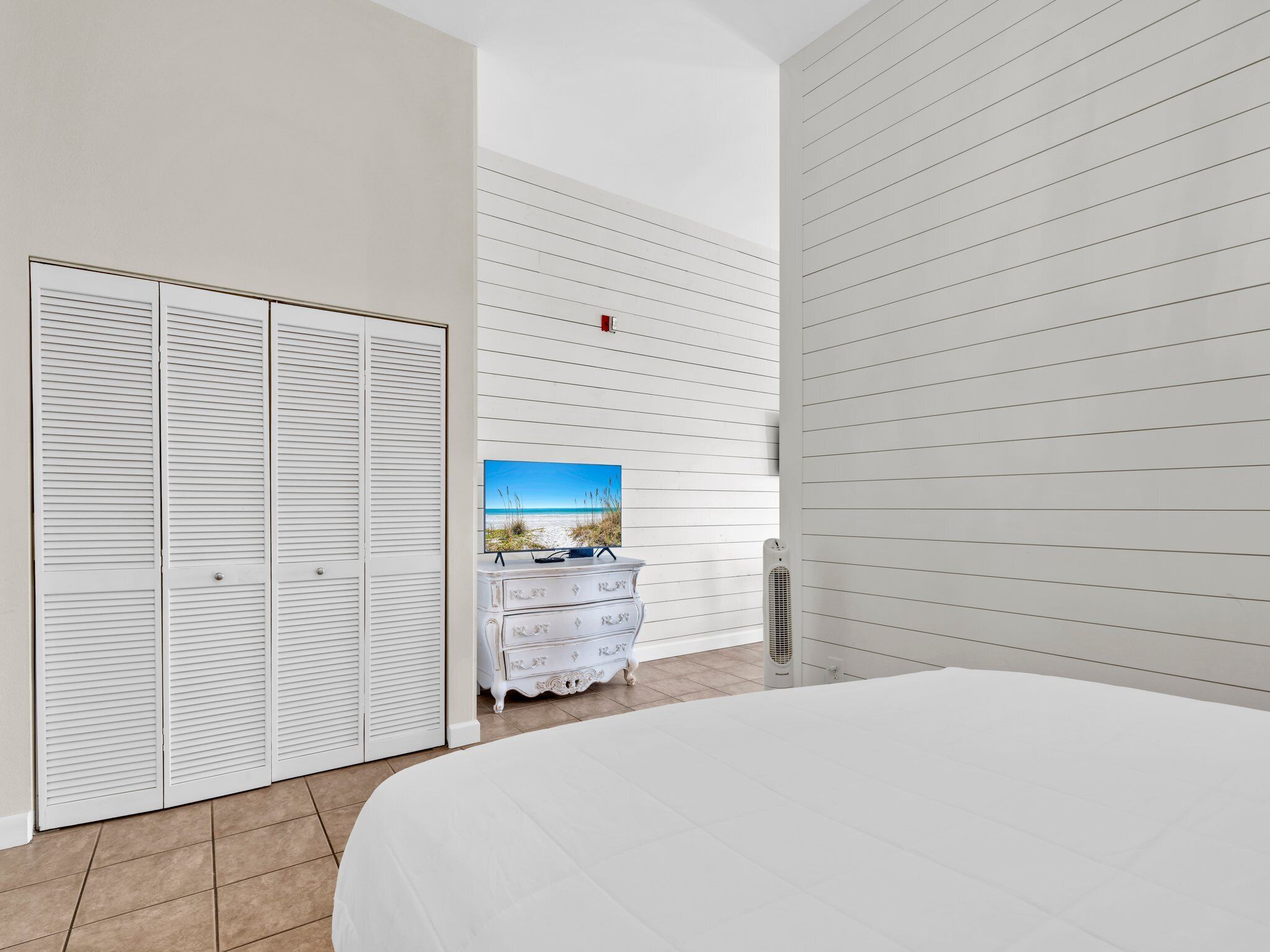 Une chambre à coucher avec un grand lit, une commode blanche, un tableau représentant une scène de plage et un radiateur.