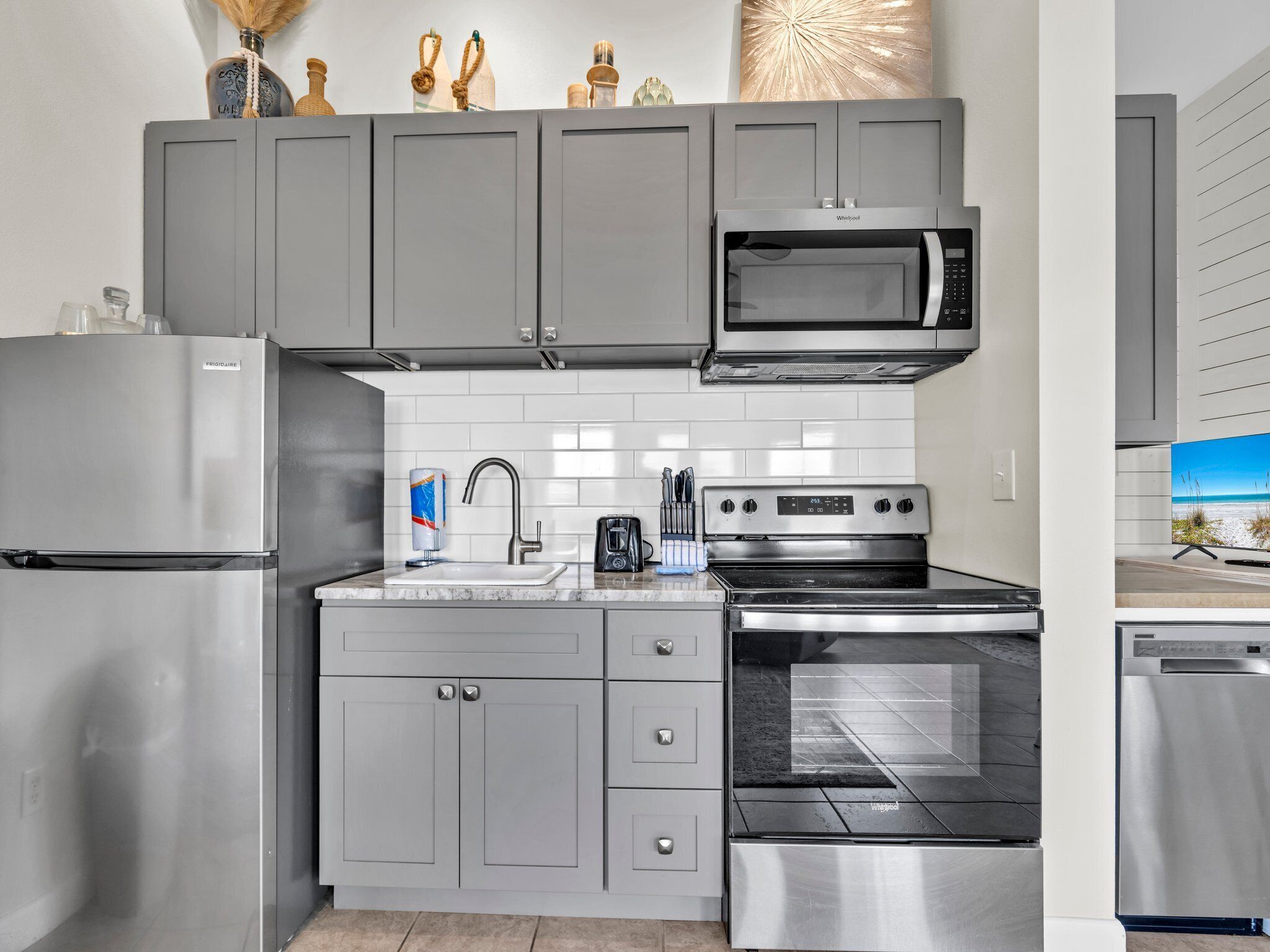 Una cocina moderna con armarios grises, un refrigerador de acero inoxidable, un microondas, una estufa y un lavavajillas.