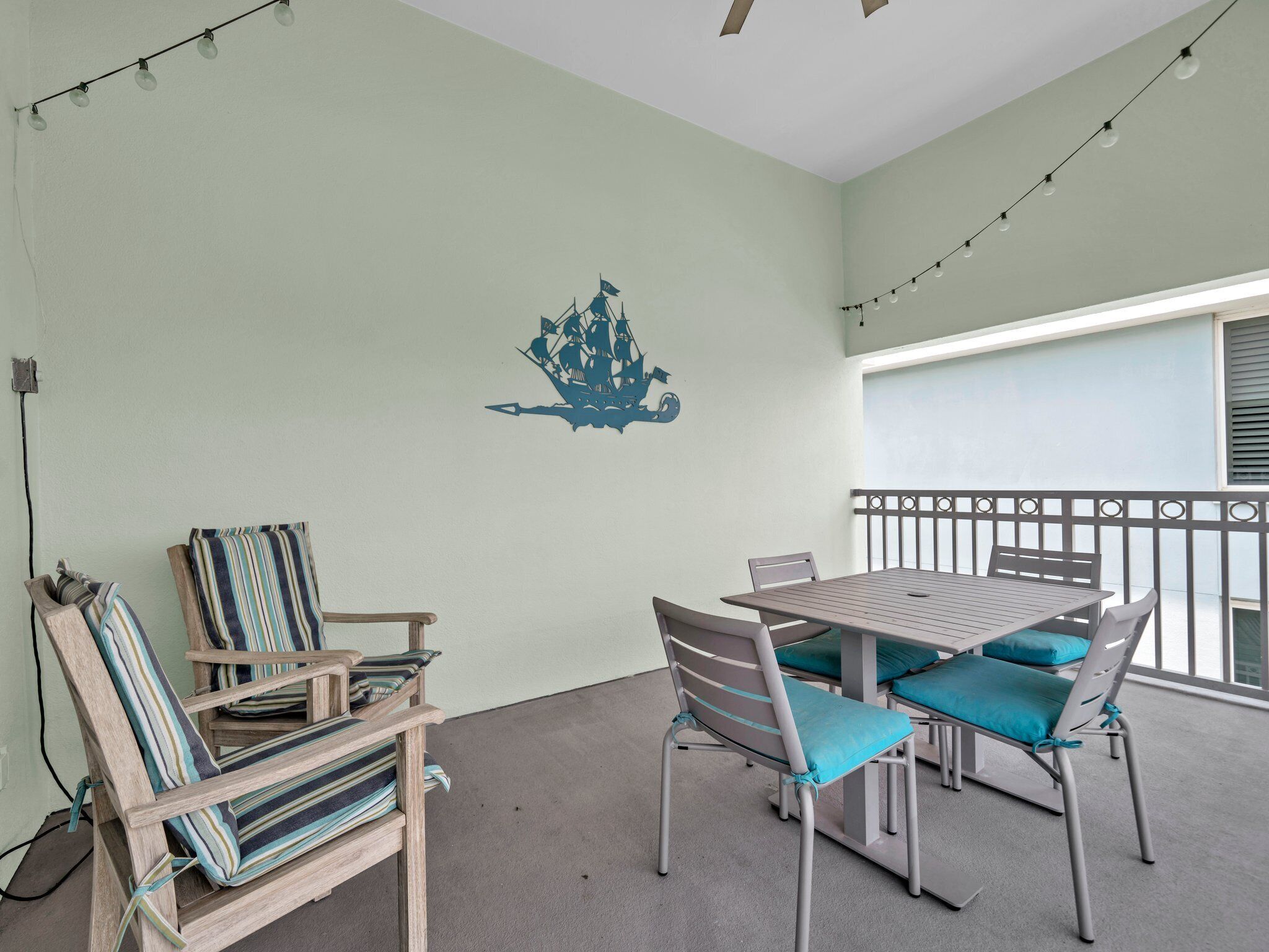 A balcony with a table and chairs, a decorative wall piece, and string lights.