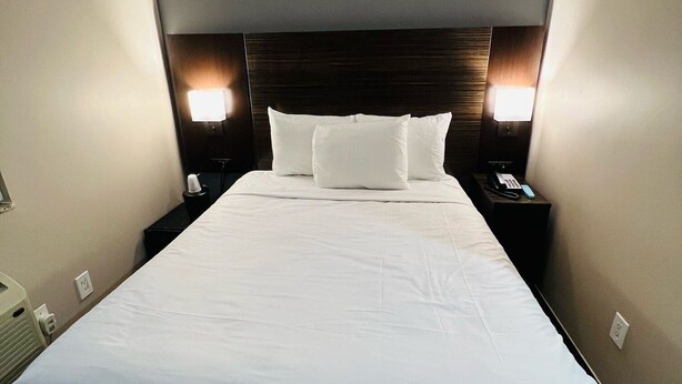 Una habitación de hotel con una cama grande, dos mesitas de noche y dos lámparas de pared.