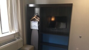 A hotel room with a bed, a TV mounted on a dark panel, a small seating area, and a waste bin. - Rockaway Hotel Brooklyn (Brooklyn)