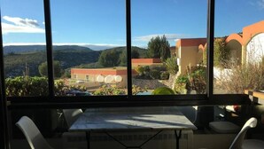 Un espace repas comprenant une table et des chaises, ainsi que de grandes fenêtres donnant sur des bâtiments et des collines.