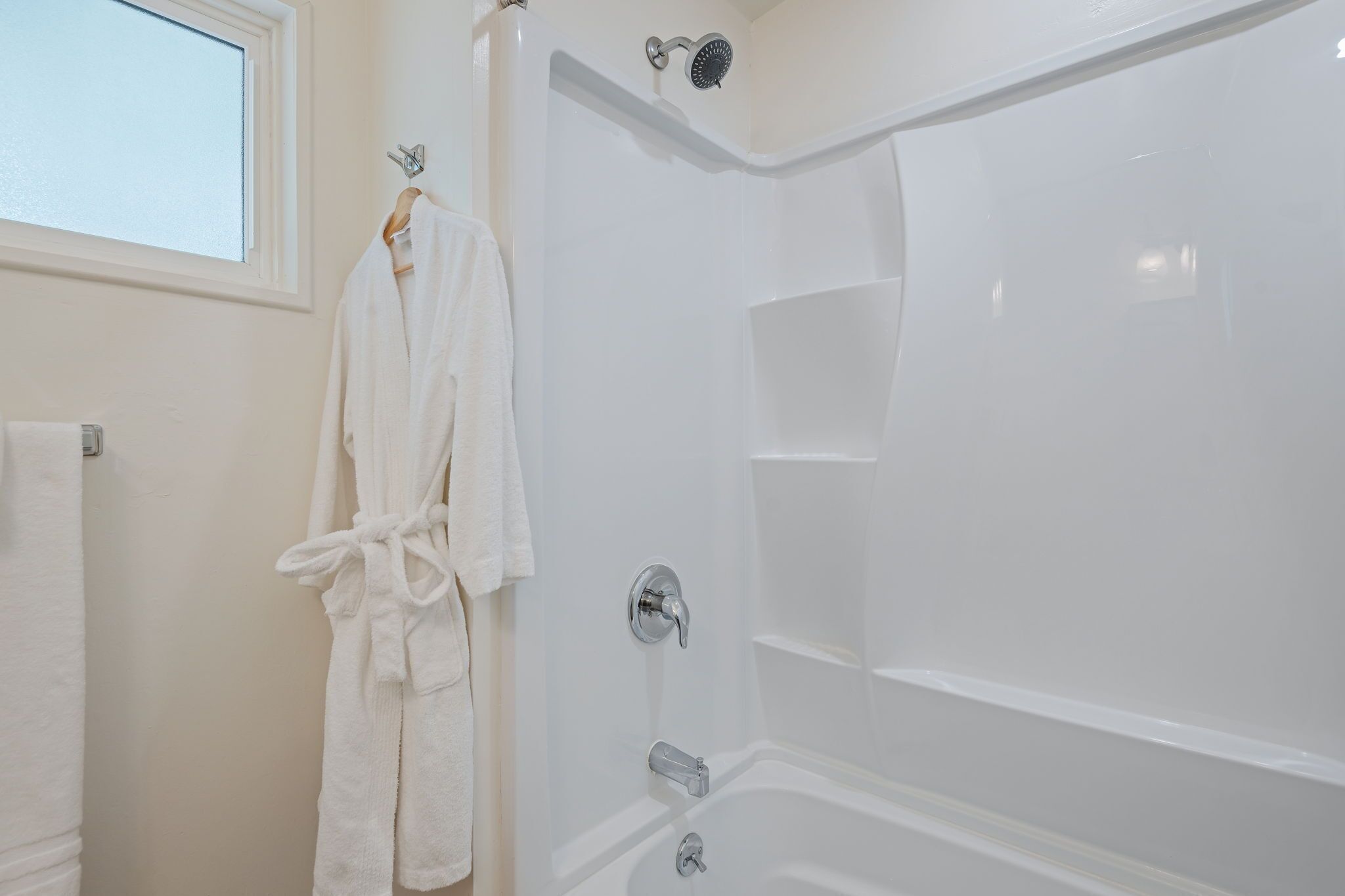 Een witte badkamer met een douche, een handdoekhouder en een raam.