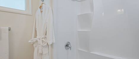 Een witte badkamer met een douche, een handdoekhouder en een raam.