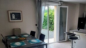 Een eethoek met een tafel en stoelen, een bar met een barkruk, en een schuifdeur die leidt naar een tuin.