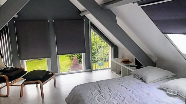 Een slaapkamer met een groot bed, dakramen en een stoel.