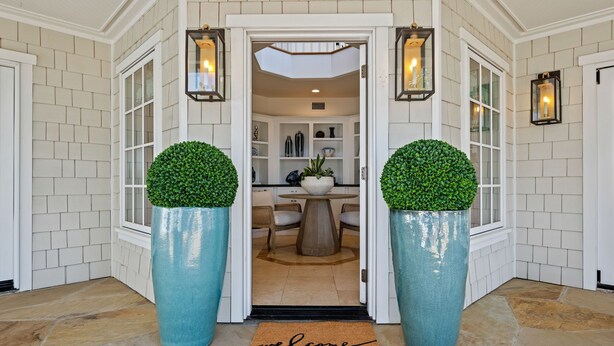 A welcoming entrance with a 'welcome' mat, a dining area with a table and chairs, and a view into a well-lit interior space. - Shoreline Splendor on the Mesa (Santa Barbara)