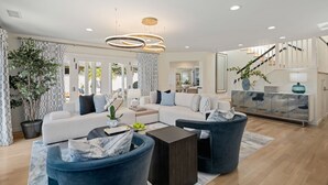 A modern living room with a white sofa, blue armchairs, and a glass cabinet. - Shoreline Splendor on the Mesa (Santa Barbara)