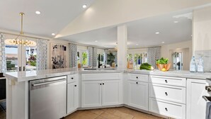 A modern kitchen with white cabinetry, a built-in dishwasher, and a large island with a sink. - Shoreline Splendor on the Mesa (Santa Barbara)