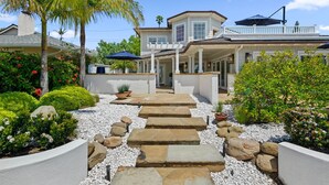 A house with a covered patio, a stone pathway, and a garden with various plants and flowers. - Shoreline Splendor on the Mesa (Santa Barbara)