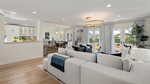 A modern living room with a large sofa, a dining area, and a kitchen in the background. - Shoreline Splendor on the Mesa (Santa Barbara)
