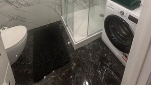 Un baño moderno con ducha de vidrio, lavadora Whirlpool y un inodoro.