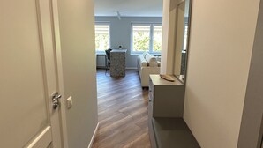 Un pasillo con una puerta a la izquierda, un banco a la derecha y vistas a una sala de estar con un sofá y una mesa.