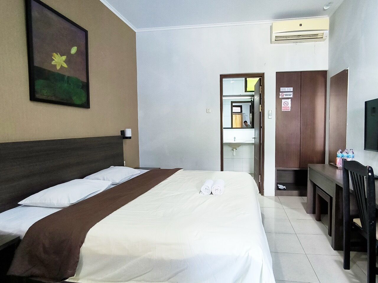 Une chambre d’hôtel avec un lit, un bureau et une chaise. On peut apercevoir la salle de bain à travers une porte ouverte.