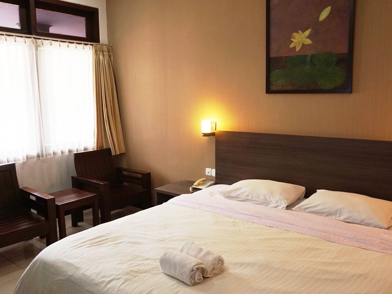A hotel room with a bed, a chair, a nightstand, a lamp, and a painting on the wall.
