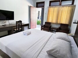 A hotel room with a bed, a desk, a chair, a TV, and a window with curtains.