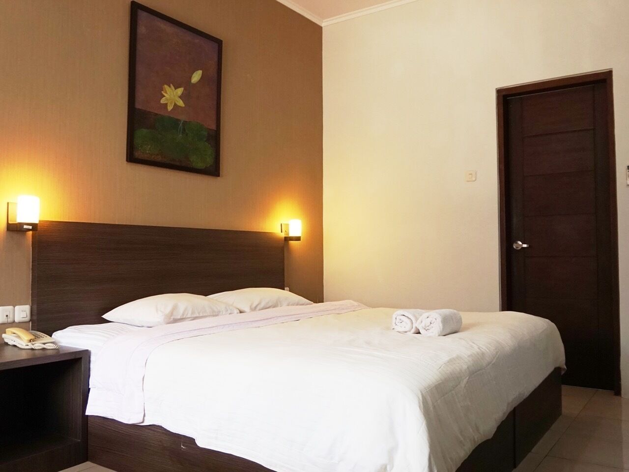 A hotel room with a large bed, two bedside lamps, a painting on the wall, and a closed door.