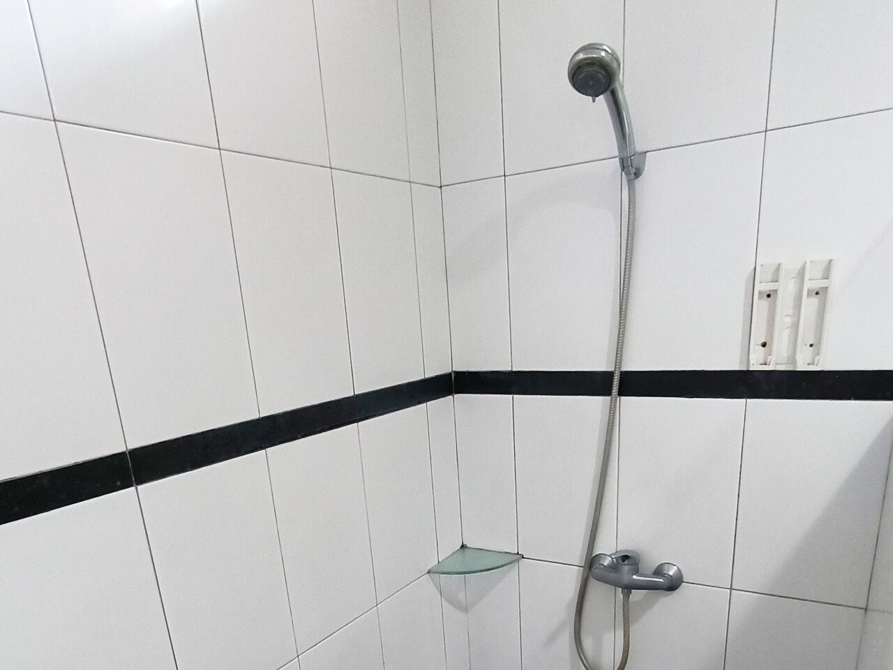 A shower area with white tiles and a black stripe, a glass shelf, and a showerhead.