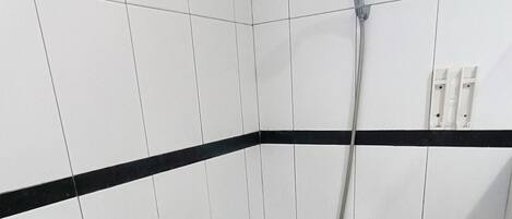 A shower area with white tiles and a black stripe, a glass shelf, and a showerhead.