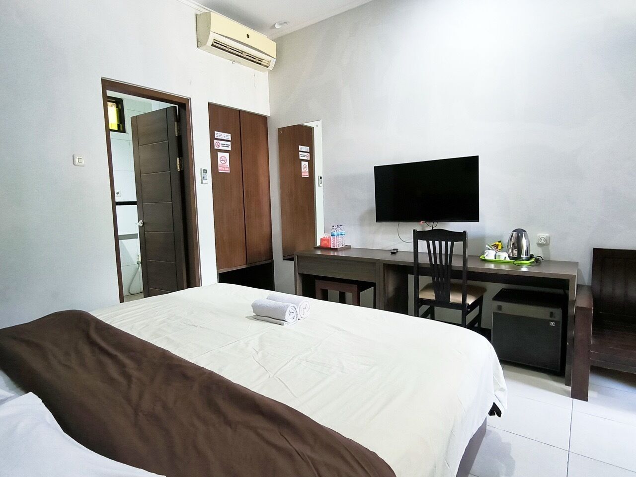 A hotel room with a bed, a desk, a chair, a television, and a wardrobe.