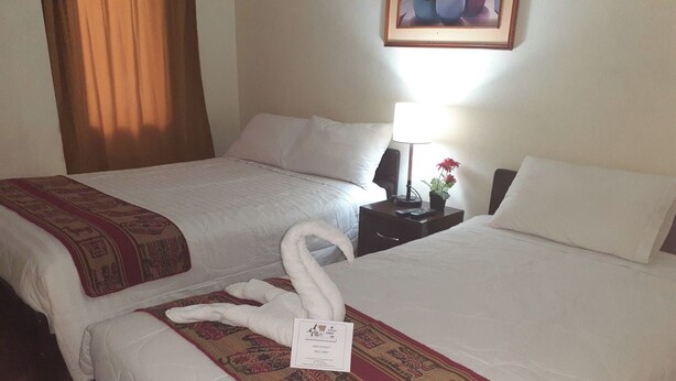 A hotel room with two beds, each with a white comforter and a red and beige patterned throw. There is a nightstand with a lamp and a small plant. - hola wellness  (Cusco)