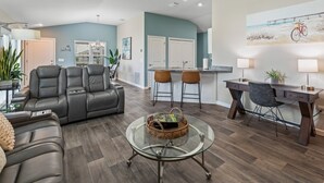 Een moderne woonkamer met een leren bank, een glazen salontafel en een eethoek met barstoelen.