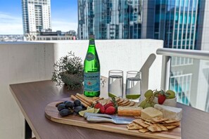 A balcony with a wooden table set with cheese, crackers, grapes, strawberries, and a bottle of Pellegrino water. - Elevate Brisbane City - Views, Pool, Sauna & Gym (Brisbane)