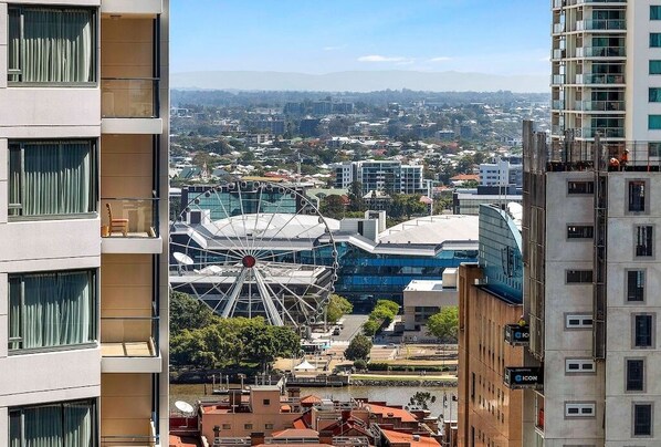 A high-rise building with multiple balconies, a Ferris wheel, and a view of a cityscape. - Elevate Brisbane City - Views, Pool, Sauna & Gym (Brisbane)