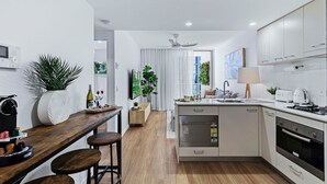 A modern kitchen with a central island, wooden bar stools, and white cabinetry.