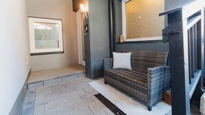 A hallway with a wicker sofa, a window with blinds, a light fixture, and a staircase.