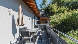 Un balcon extérieur avec une table et des chaises, un parasol suspendu et une rambarde.