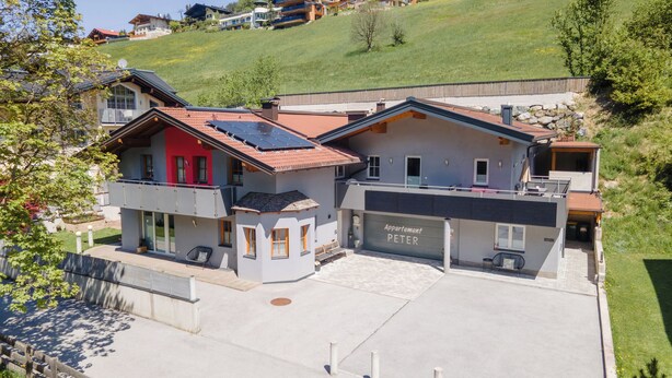 Une maison moderne à deux étages, avec un toit recouvert de tuiles rouges, un garage et un espace extérieur aménagé avec un coin salon abrité.