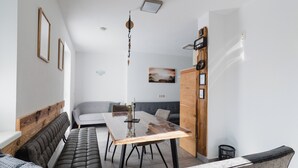 A modern living room with a wooden dining table, a grey sofa, and a black leather bench.
