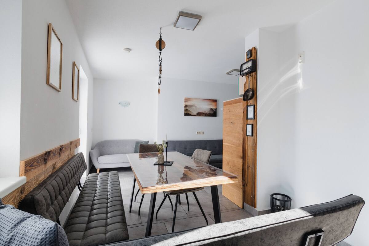 Un soggiorno moderno con un tavolo da pranzo in legno, un divano grigio e una panca in pelle nera.