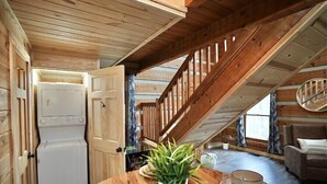 Un acogedor cuarto ático con techo de madera, lavadora integrada, una mesa de comedor con platos y vasos, y una escalera.